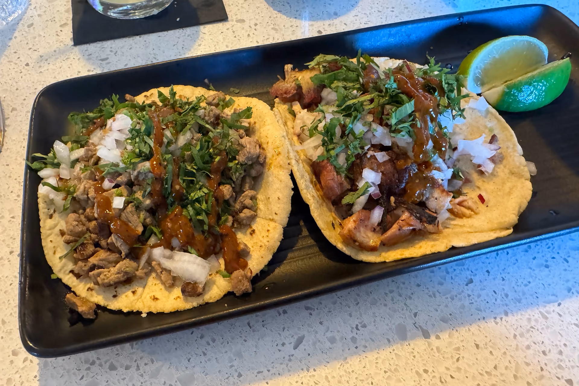 Demo sample photo: two street tacos, one carnitas and one carne asada, with onion, cilantro and lime on a black tray.